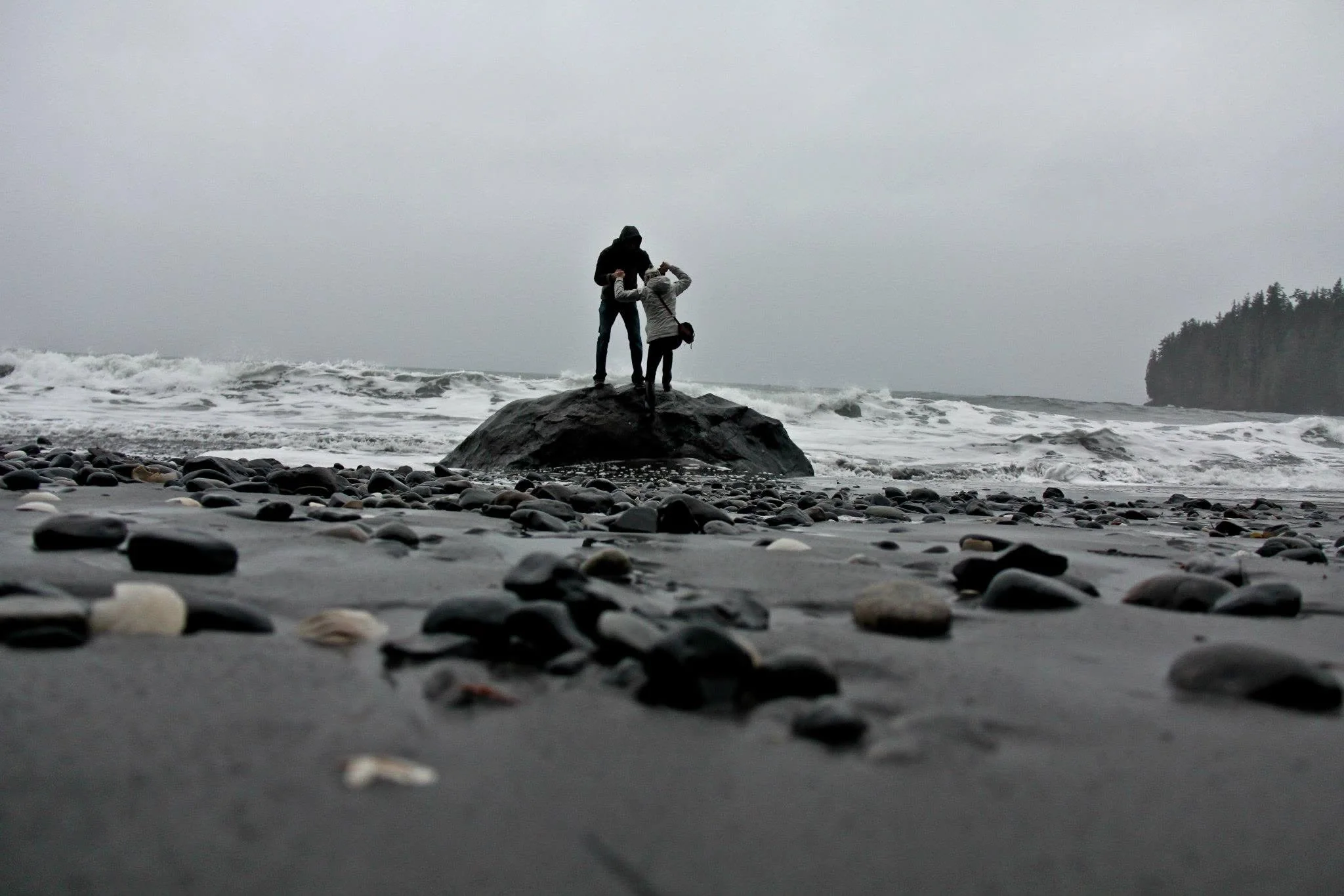 Owen and Megan standing together on a rock above a winter beach