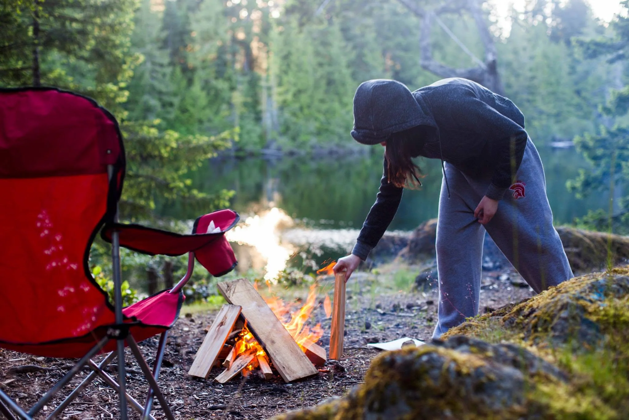 Megan tending a campfire beside a forest lake