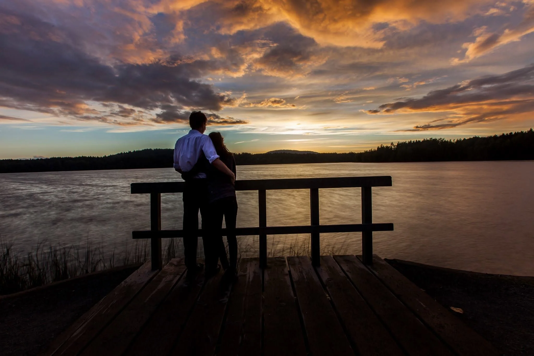 Owen and Megan embracing on a dock beneath a dramatic sunset
