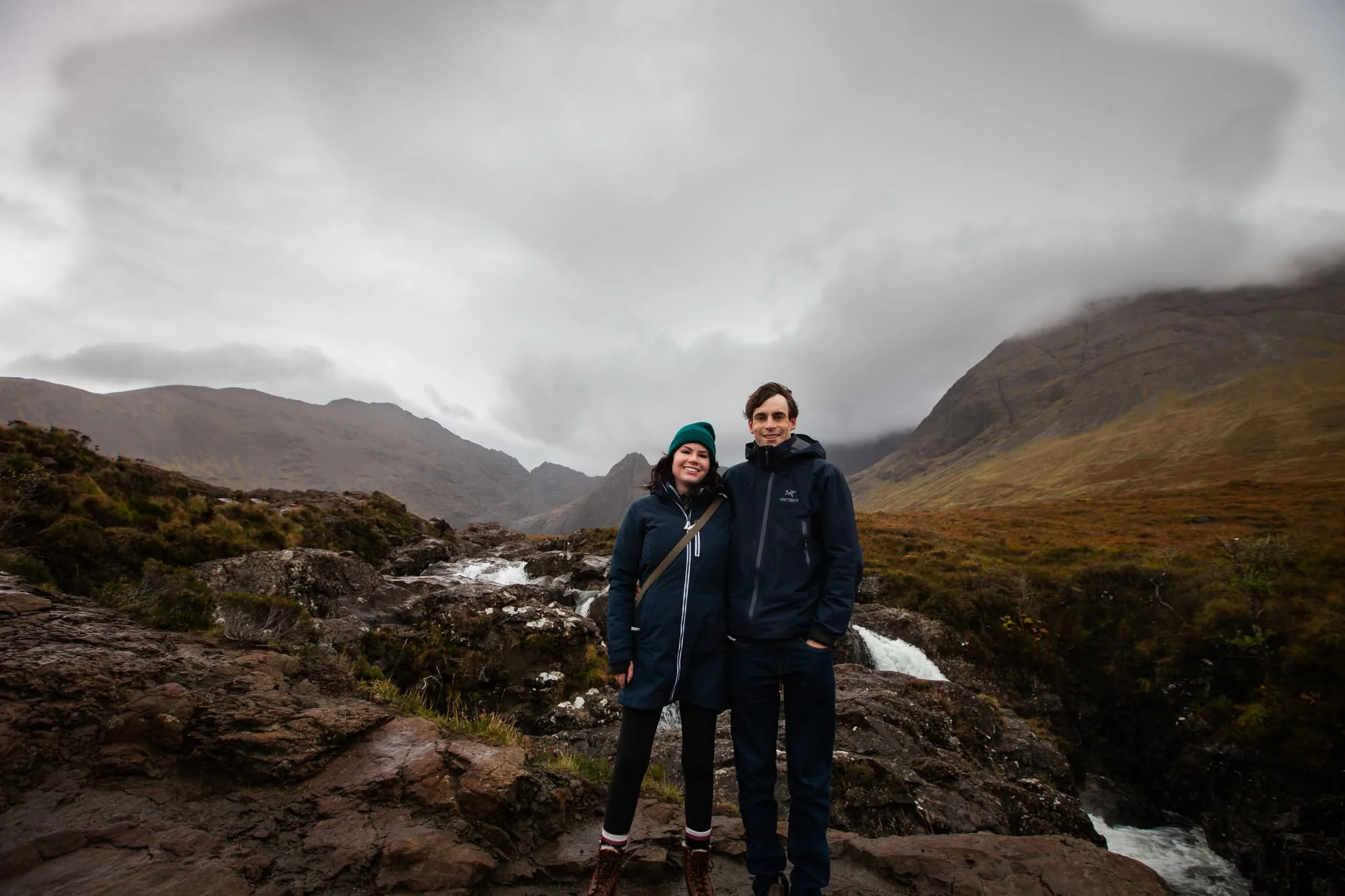 Owen and Megan standing together at the Fairy Pools beneath the Cuillin mountains on the Isle of Skye
